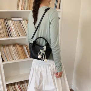 Black faux leather bucket bag with pearl tulip bow charm shown worn over shoulder