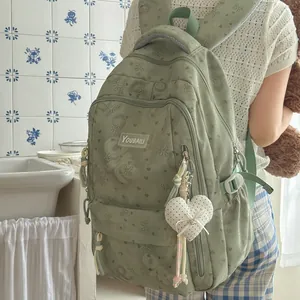 Detailed view of a sage green floral backpack with a cute heart plush pendant charm.