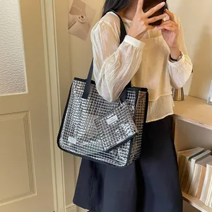 Reflective silver grid patterned tote bag with matching small pouch carried by a person indoors