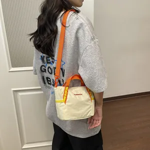 Detail of a cream quilted tote bag with vibrant orange handles and shoulder strap