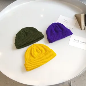 Top-down view of three colorful short knitted beanie hats on a minimalist white table