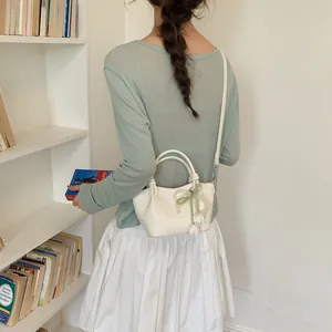 Cream vintage bucket bag with pearl bow detail worn as a crossbody by a female model
