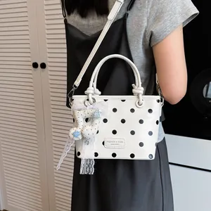 Close-up of stylish white polka dot handbag with lace music note charm detail.