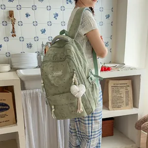 Detail view of a sage green patterned backpack with a cute heart pendant charm.