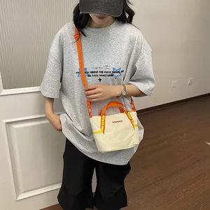 Model showcasing a stylish off-white textile crossbody bag with vibrant orange straps