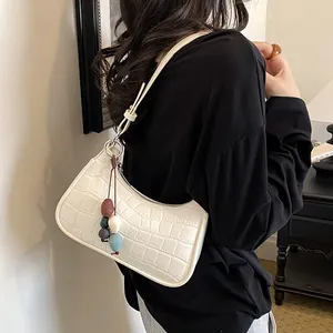 White crocodile pattern dumpling bag with colorful bead tassel charm in a lifestyle setting