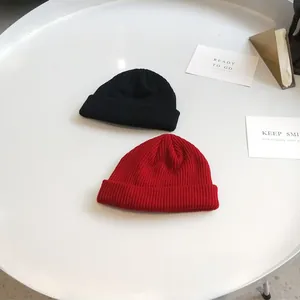 Top view of black and red ribbed knit short beanies on a minimalist white surface