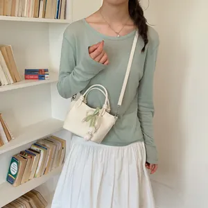 Detailed view of a cream crossbody bucket bag featuring a pearl bow and floral charm accessory