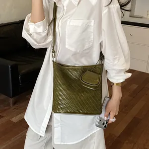 Lifestyle view of an olive green woven bucket bag with a matching mini pouch charm