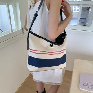 Detailed view of a striped canvas tote bag worn by a model in a bright indoor room