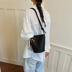 Model trägt eine schwarze geflochtene Beuteltasche mit schickem Perlenanhänger