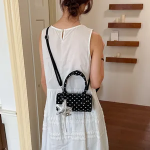 Stylish black polka dot cylinder handbag with star charm shown on model in a white dress.