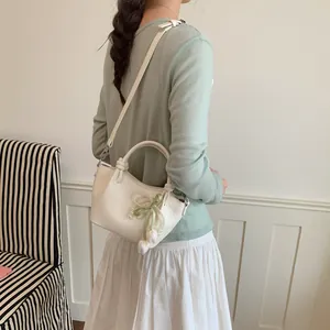 Detailed shot of cream crossbody handbag featuring pearl and bow accents on model
