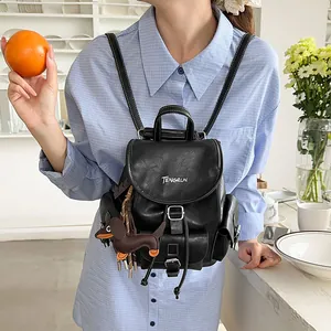 Small black minimalist commuter backpack with dog charm worn by model in a cafe