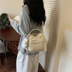 Elegante beige Umhängetasche im Nischen-Design mit Plüsch-Anhänger und Gittermuster.