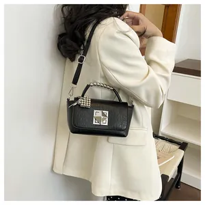 Close-up of stylish black square handbag with silver metallic details on white blazer