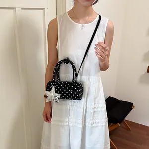 Detail shot of a black polka dot cylinder crossbody bag worn with a white dress