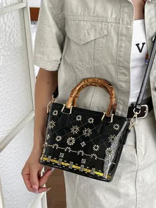 Elegant black patent leather handbag featuring bamboo handles and intricate floral stud details