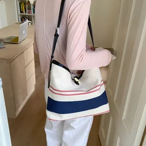 Large striped canvas tote bag with navy and red accents worn by a person in a room