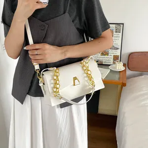 Detail shot of an elegant white crossbody bag with a gold chain and metal clasp