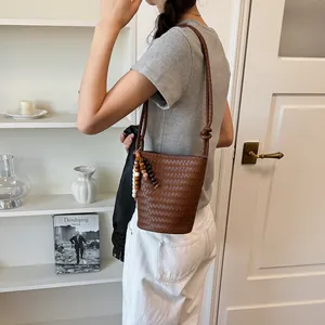 Detailansicht einer braunen geflochtenen Beuteltasche mit Perlenanhänger am Modell