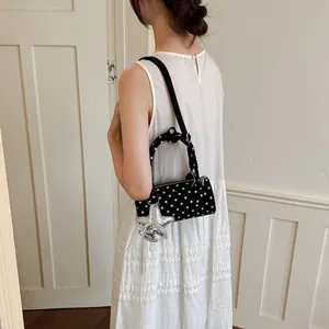 Detailed view of black polka dot cylindrical handbag with silver star charm on a model