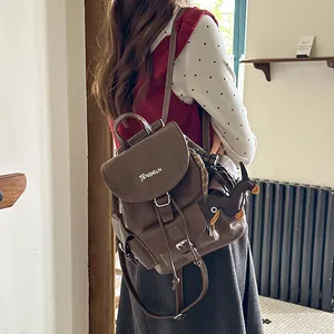 Detail of a brown leather commuter backpack with a stylish dachshund charm on a model.