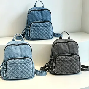 Drei modische gesteppte Denim-Rucksäcke in Blau und Grau auf einem minimalistischen weißen Ständer