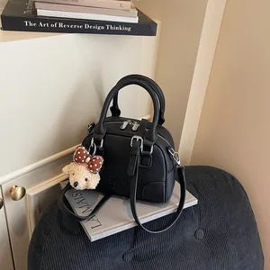 Close-up of a black pebbled leather Boston bag with a cute bear charm on a stack of books.