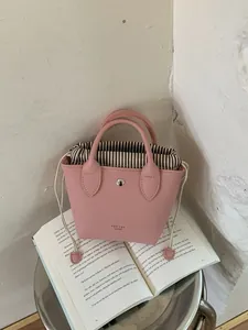 Petit sac seau rose élégant avec doublure à cordon rayé sur un livre.