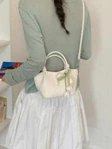 Elegant cream bucket shoulder bag featuring a pearl bow charm and textured finish on a model