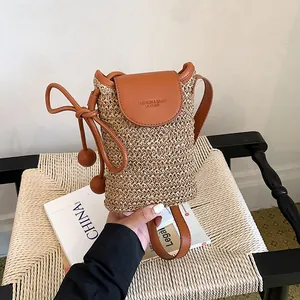 Handheld close-up of a stylish woven straw crossbody phone bag with leather flap.