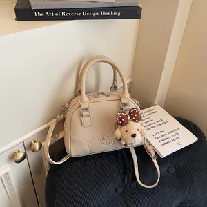 High-end beige lychee pattern Boston handbag for women with a cute bear charm accessory.