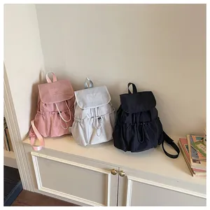 Three drawstring pleated backpacks in pink, grey, and black on a white bench.