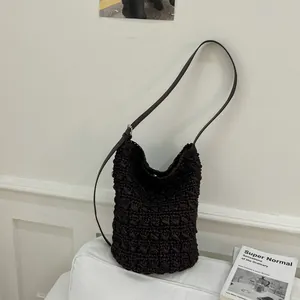 Dunkelbraune geflochtene Stroh-Eimertasche mit schmalem Lederriemen auf weißem Sofa
