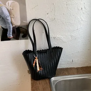 Detailed view of a black woven tote bag with scalloped edges and a decorative bead charm