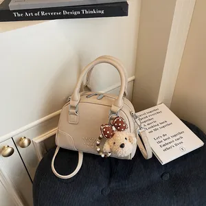Detail view of a khaki Boston handbag featuring a teddy bear charm and premium textured leather.