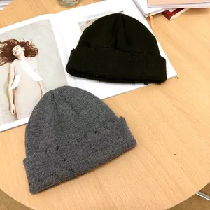 Vue détaillée de deux bonnets en tricot usés gris et vert foncé sur une table en bois.