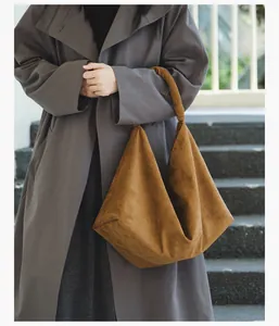 Woman carrying a large camel suede hobo bag styled with a grey coat outdoors
