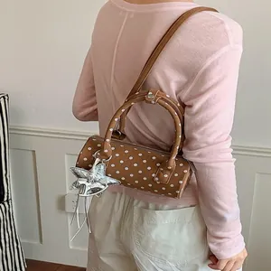 Stylish brown polka dot cylinder handbag with star charm, presented on a model's shoulder