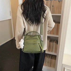 Detaillierte Rückansicht einer Frau mit einer grün karierten Umhängetasche in einer Bibliothek
