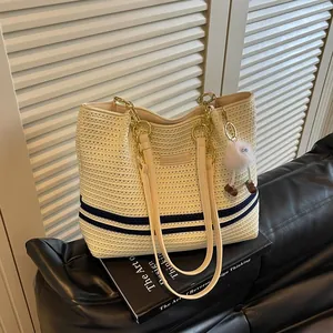 Detailed view of a cream woven tote bag with navy stripes and gold chain straps