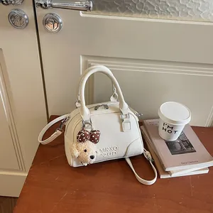 Close-up of a white pebbled leather Boston handbag with a plush dog charm on a wooden table