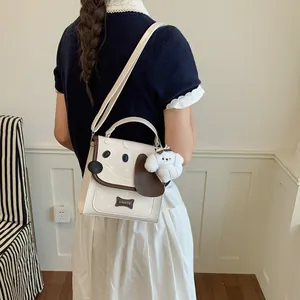 Cute cream-colored dog-themed crossbody bag with plush charm accessory worn by a model
