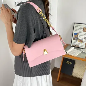 Detail shot of pink small square shoulder bag with gold chain strap worn by model.