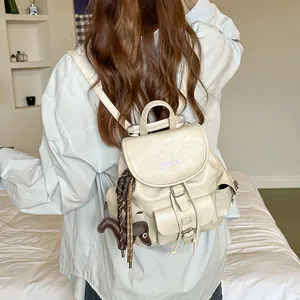 Back view of a woman wearing a stylish cream faux leather mini backpack with a dog charm