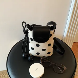 Detail of a minimalist polka dot crossbody phone bag with leather flap and rope strap