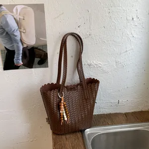 Detailed view of dark brown woven bucket bag with beaded charm in a retro rustic scene