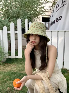 Gros plan d'une femme portant un chapeau cloche à fleurs vertes dans un jardin.