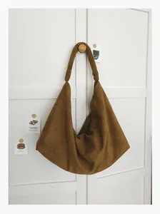 Close-up view of a minimalist brown suede large capacity hobo bag hanging on a white door